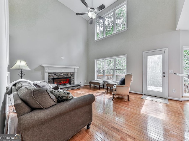 living room featuring a wealth of natural light, light hardwood / wood-style floors, a stone fireplace, and a high ceiling