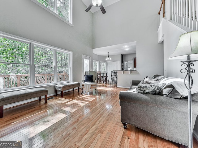 living room with light wood-type flooring, a high ceiling, and ceiling fan with notable chandelier