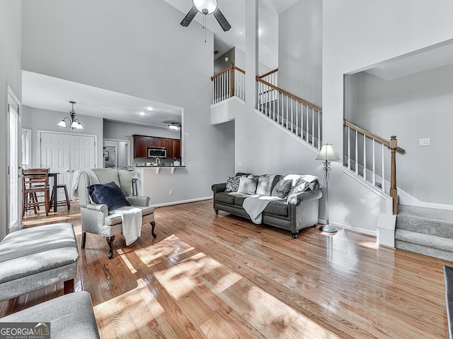 living room featuring ceiling fan with notable chandelier, light wood-type flooring, and a towering ceiling