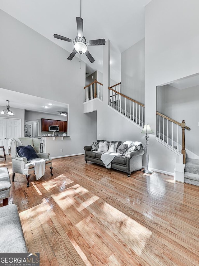 living room with ceiling fan with notable chandelier, light wood-type flooring, and a high ceiling