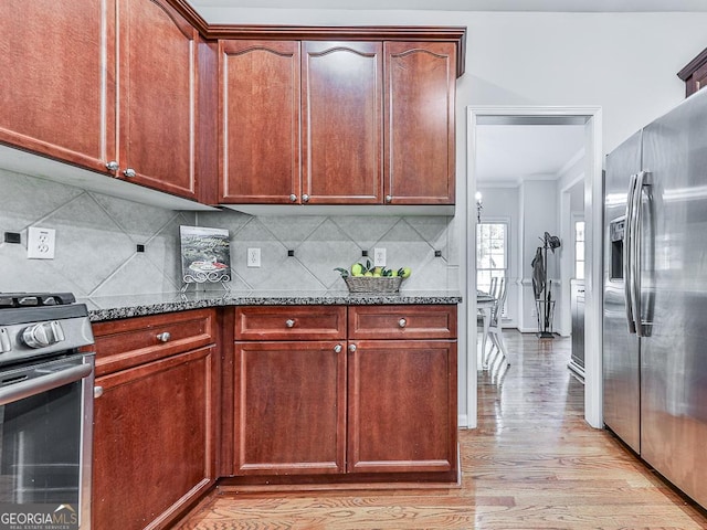 kitchen featuring backsplash, dark stone countertops, ornamental molding, appliances with stainless steel finishes, and light hardwood / wood-style floors