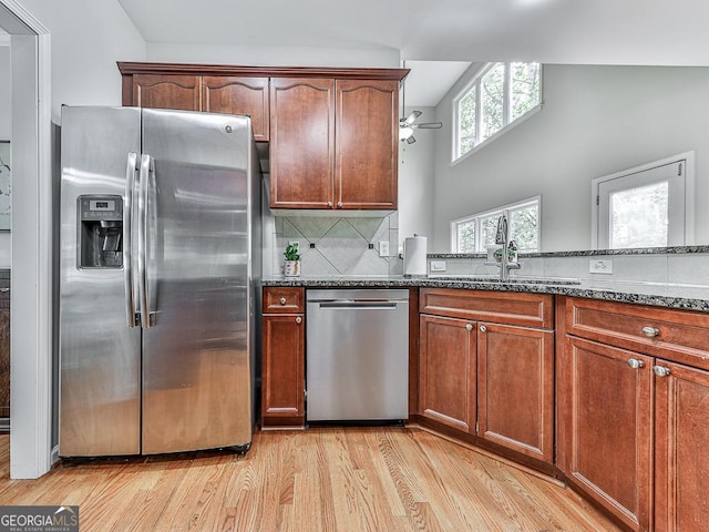 kitchen featuring appliances with stainless steel finishes, light wood-type flooring, tasteful backsplash, dark stone counters, and ceiling fan