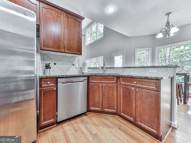 kitchen with stainless steel appliances, tasteful backsplash, a notable chandelier, dark stone counters, and decorative light fixtures