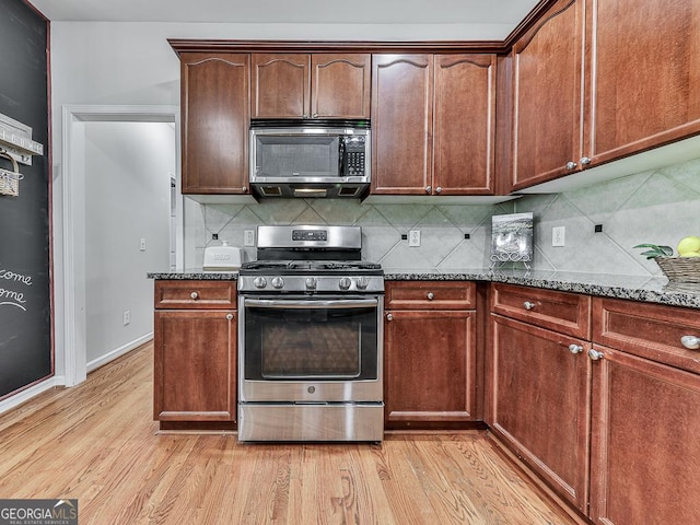 kitchen with decorative backsplash, dark stone countertops, light wood-type flooring, and stainless steel appliances