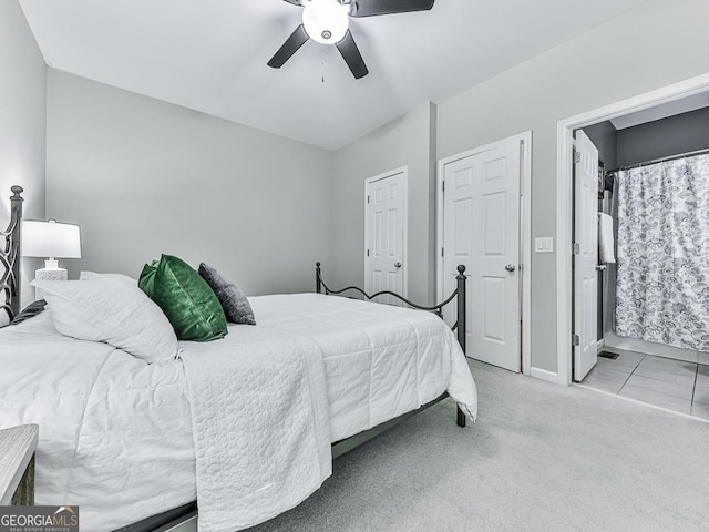 bedroom with ceiling fan, light colored carpet, and ensuite bath