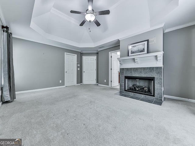 unfurnished living room featuring carpet flooring, ceiling fan, a raised ceiling, a tiled fireplace, and ornamental molding