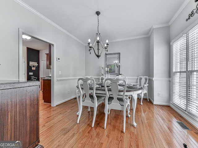 dining area with crown molding, an inviting chandelier, and light wood-type flooring