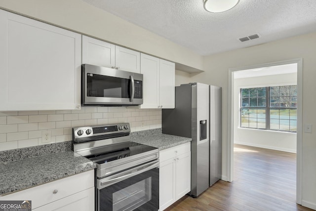 kitchen featuring light stone countertops, white cabinetry, a textured ceiling, and appliances with stainless steel finishes