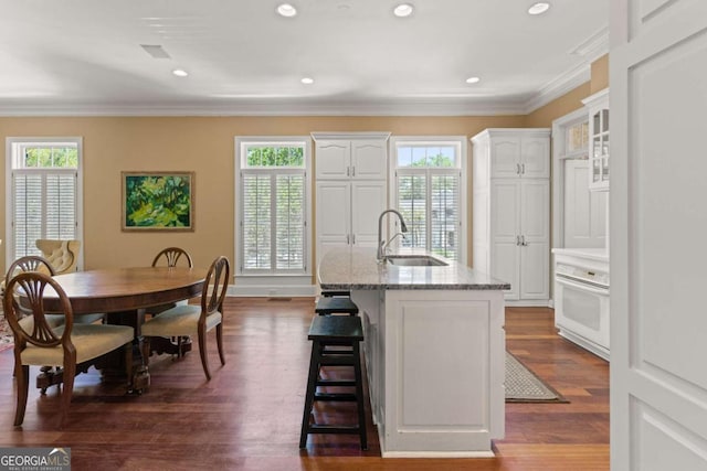 kitchen with a kitchen bar, dark wood-type flooring, sink, a center island with sink, and white cabinets