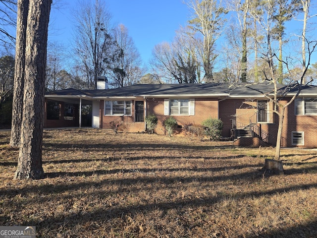 ranch-style house featuring an attached carport, brick siding, a chimney, and a front lawn