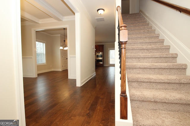 stairs with hardwood / wood-style flooring, crown molding, and an inviting chandelier