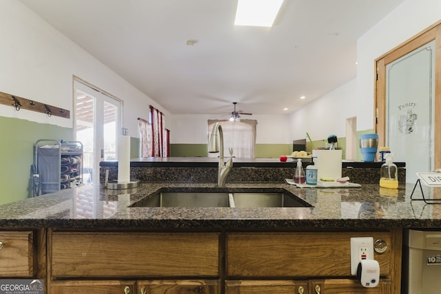 kitchen featuring ceiling fan, dark stone counters, and sink