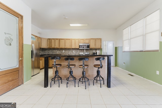 kitchen with a kitchen bar, tasteful backsplash, stainless steel appliances, a center island, and light tile patterned flooring