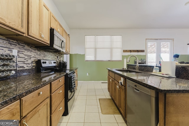 kitchen with appliances with stainless steel finishes, tasteful backsplash, dark stone counters, sink, and light tile patterned floors