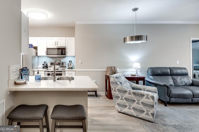 kitchen with a kitchen breakfast bar, light wood-type flooring, appliances with stainless steel finishes, decorative light fixtures, and white cabinetry