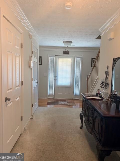 carpeted foyer entrance with a textured ceiling and ornamental molding