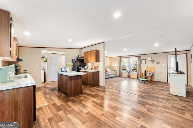 kitchen with crown molding, black refrigerator, a center island, and light wood-type flooring