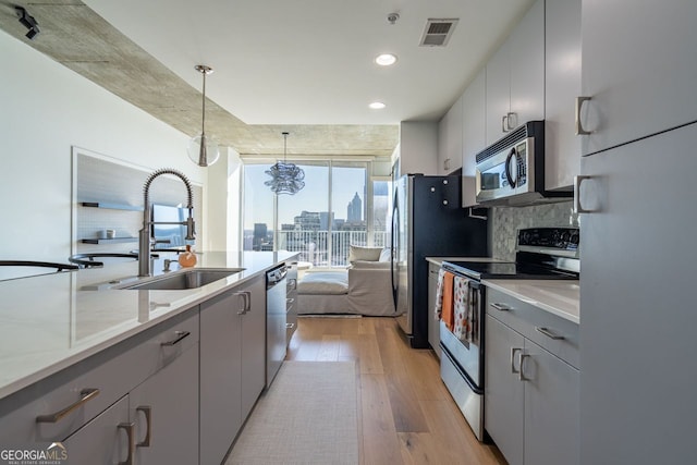 kitchen with pendant lighting, appliances with stainless steel finishes, sink, light wood-type flooring, and gray cabinets