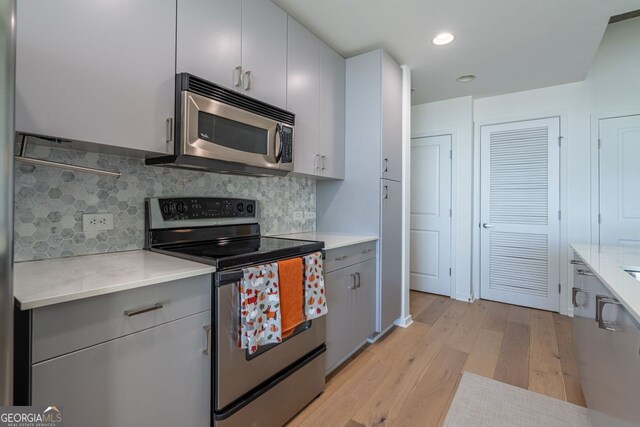 kitchen with white cabinets, appliances with stainless steel finishes, tasteful backsplash, light wood-type flooring, and gray cabinetry