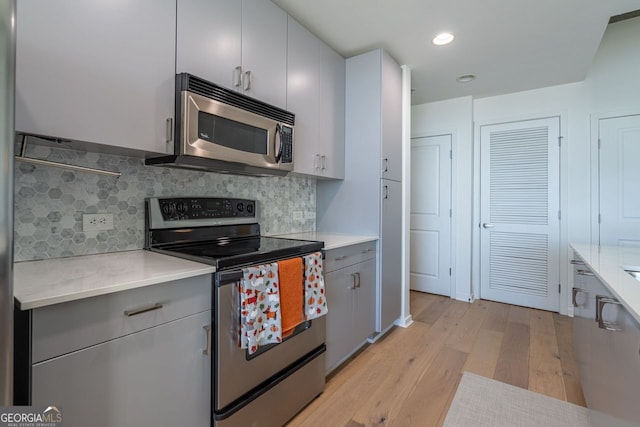 kitchen featuring stainless steel appliances, light wood finished floors, gray cabinets, and light countertops