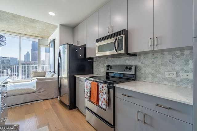 kitchen with stainless steel appliances, light countertops, light wood-style flooring, decorative backsplash, and gray cabinetry