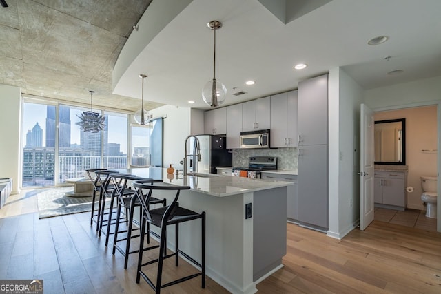 kitchen featuring light hardwood / wood-style floors, appliances with stainless steel finishes, a wall of windows, sink, and decorative light fixtures