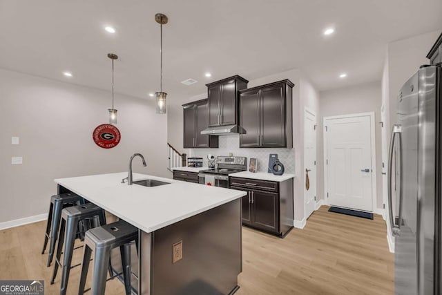 kitchen featuring stainless steel appliances, a kitchen island with sink, sink, decorative light fixtures, and light hardwood / wood-style floors