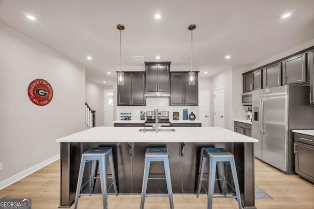 kitchen featuring pendant lighting, sink, stainless steel fridge, an island with sink, and light hardwood / wood-style floors