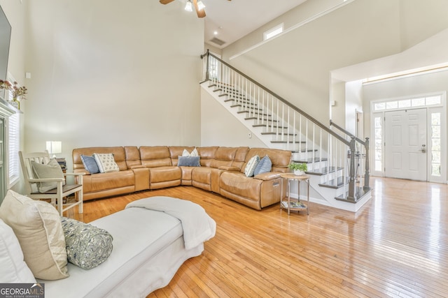 living room with a towering ceiling, hardwood / wood-style flooring, and ceiling fan