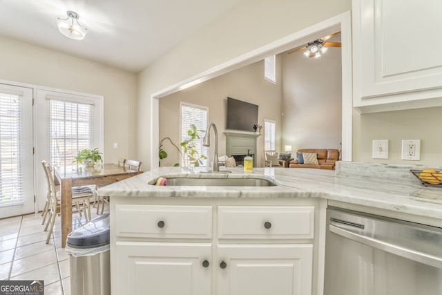 kitchen featuring light stone counters, stainless steel dishwasher, sink, light tile patterned floors, and white cabinets