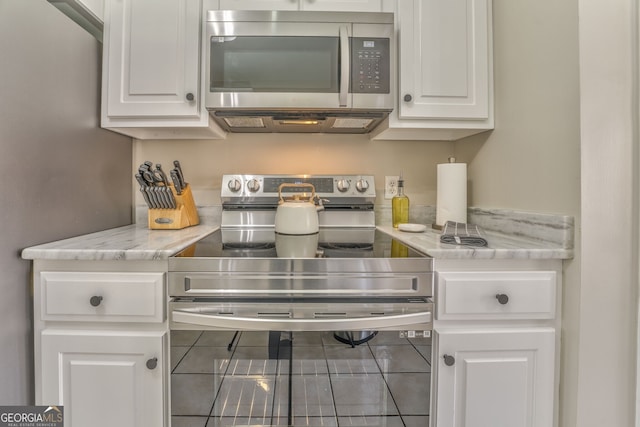 kitchen with appliances with stainless steel finishes, white cabinetry, tile patterned floors, and light stone counters