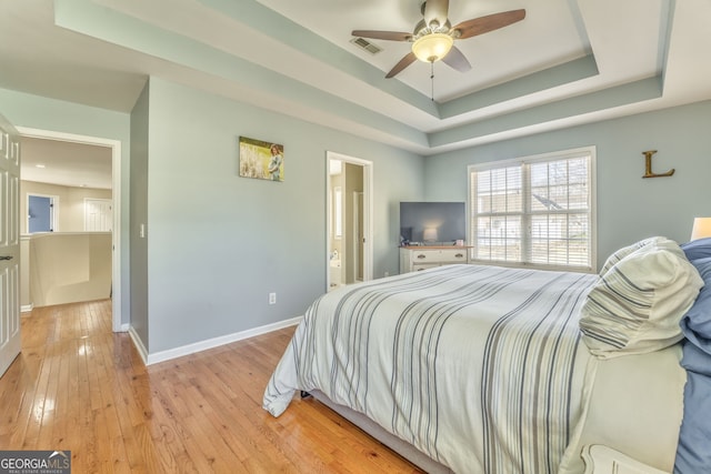 bedroom with ensuite bath, a raised ceiling, ceiling fan, and light hardwood / wood-style floors