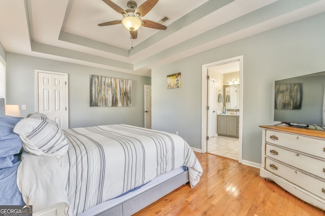 bedroom with ensuite bathroom, a raised ceiling, ceiling fan, light hardwood / wood-style flooring, and a closet