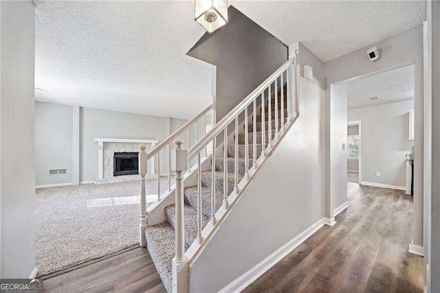 staircase featuring a fireplace, wood-type flooring, and a textured ceiling