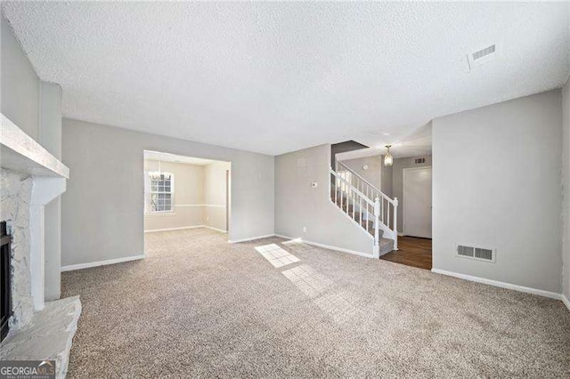 unfurnished living room featuring a stone fireplace, carpet floors, and a textured ceiling