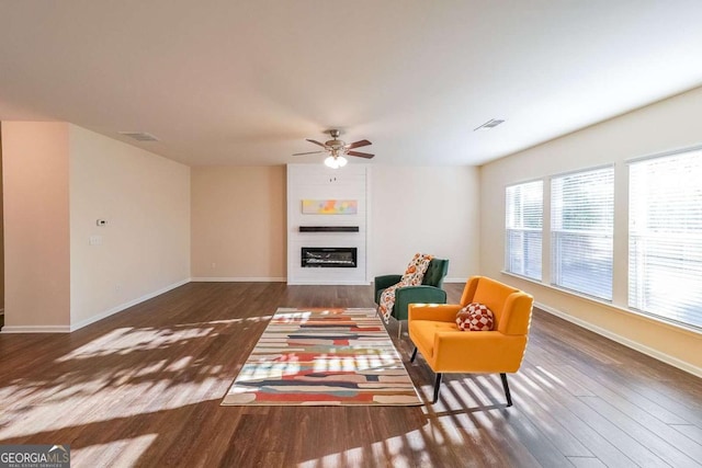 living area featuring ceiling fan, a fireplace, and dark wood-type flooring