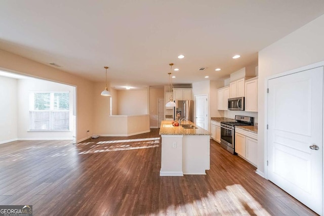 kitchen featuring appliances with stainless steel finishes, decorative light fixtures, white cabinetry, and an island with sink