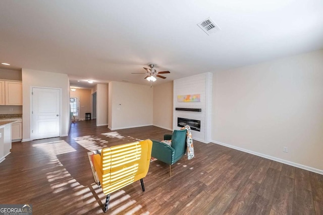 living room with ceiling fan, a large fireplace, and dark hardwood / wood-style flooring