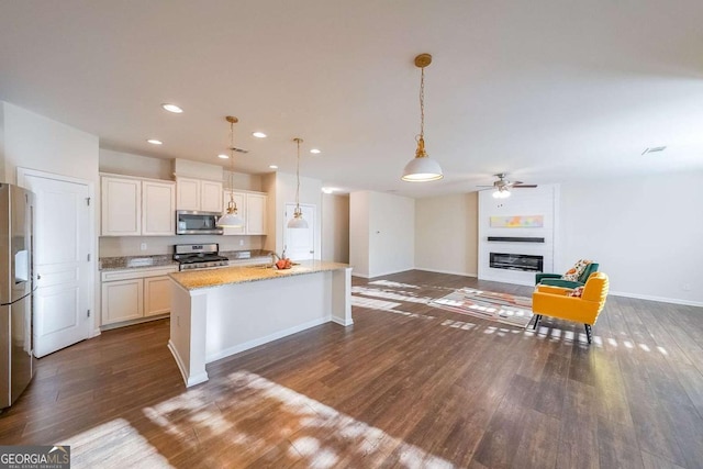 kitchen with a large fireplace, stainless steel appliances, white cabinetry, hanging light fixtures, and an island with sink