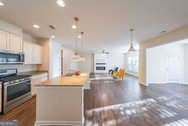 kitchen with light stone countertops, sink, stainless steel appliances, pendant lighting, and a kitchen island with sink