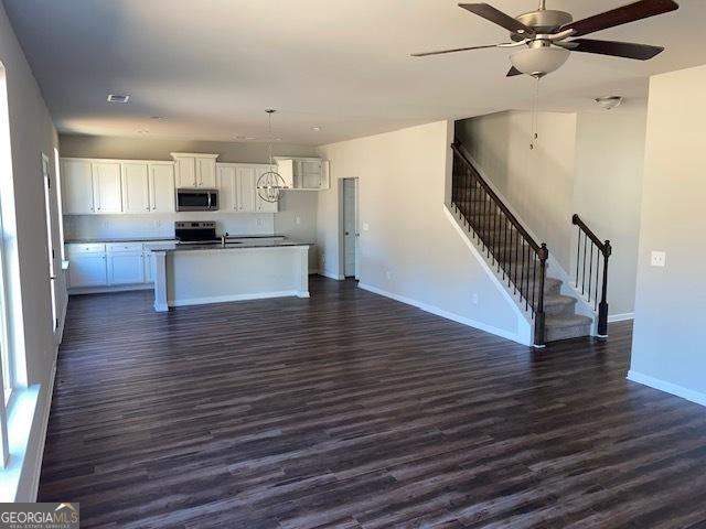 kitchen with stove, a center island with sink, white cabinetry, and dark wood-type flooring