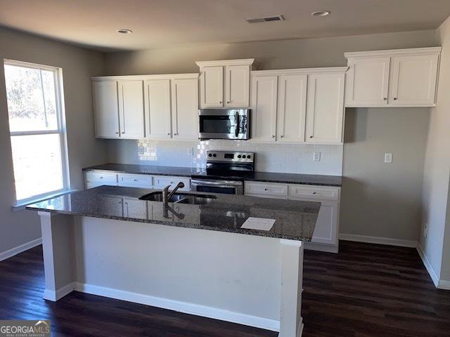 kitchen featuring white cabinets, appliances with stainless steel finishes, a center island with sink, and sink