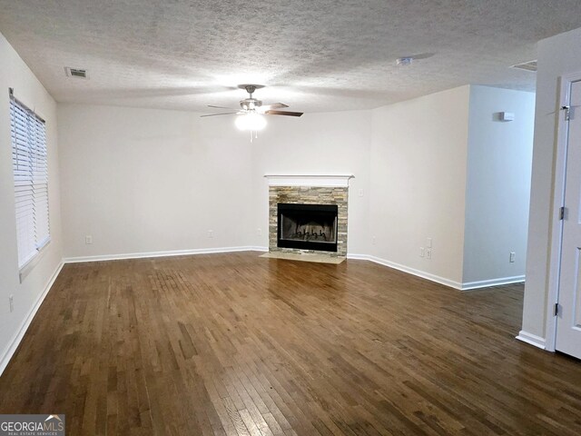 unfurnished living room featuring dark hardwood / wood-style flooring, ceiling fan, a fireplace, and a textured ceiling