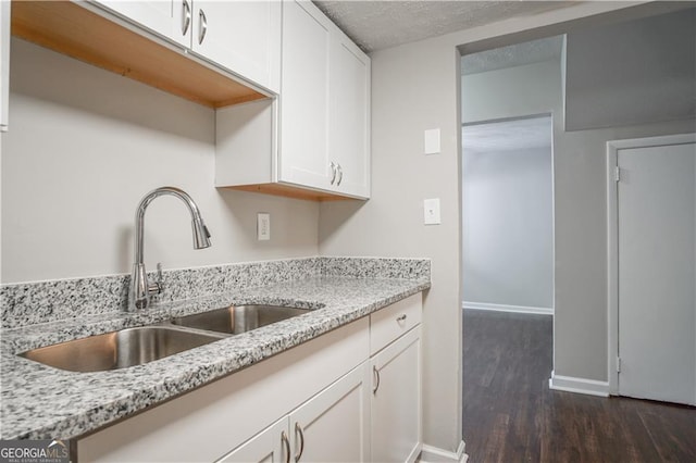 kitchen with light stone countertops, sink, dark wood-type flooring, and white cabinets