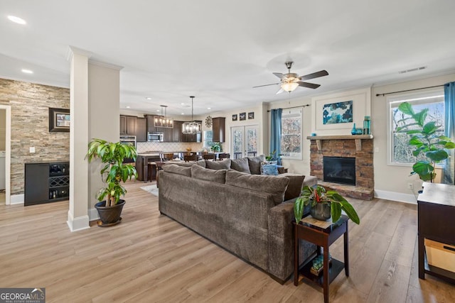 living room featuring a wealth of natural light, a fireplace, ceiling fan with notable chandelier, and light hardwood / wood-style flooring