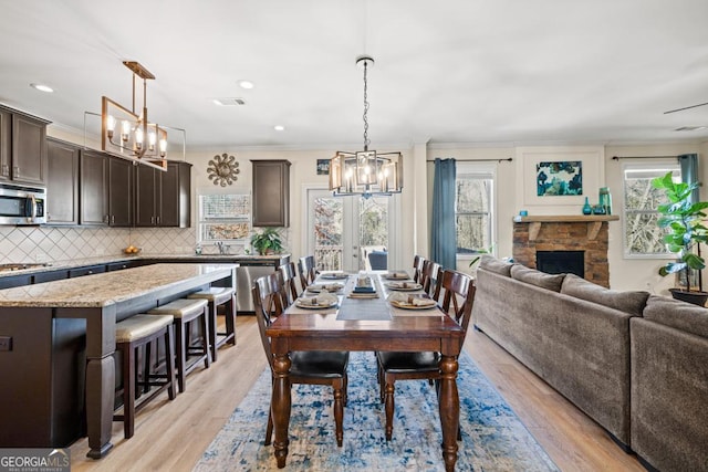 dining area featuring a stone fireplace, crown molding, plenty of natural light, and light hardwood / wood-style flooring