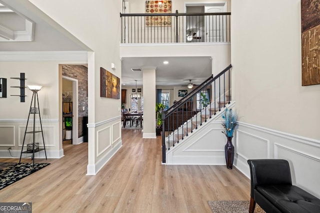 foyer featuring a towering ceiling, light hardwood / wood-style floors, and ceiling fan with notable chandelier