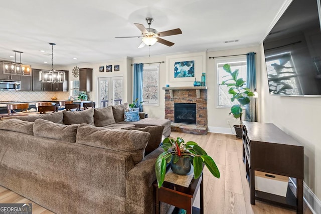 living room featuring a stone fireplace, light hardwood / wood-style floors, ceiling fan with notable chandelier, and ornamental molding