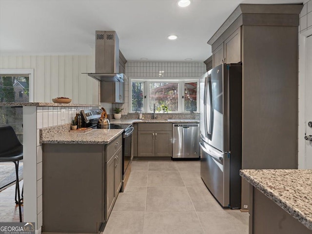 kitchen featuring light stone countertops, appliances with stainless steel finishes, sink, wall chimney range hood, and light tile patterned floors