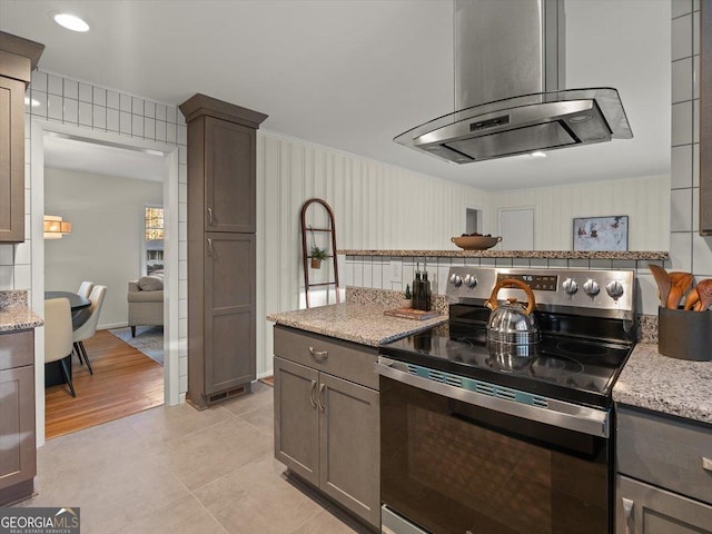 kitchen featuring island exhaust hood, light tile patterned floors, stainless steel electric range oven, and light stone counters